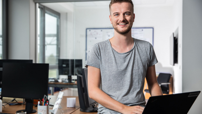 Junger Mann mit Laptop sitzt auf Tisch im Büro