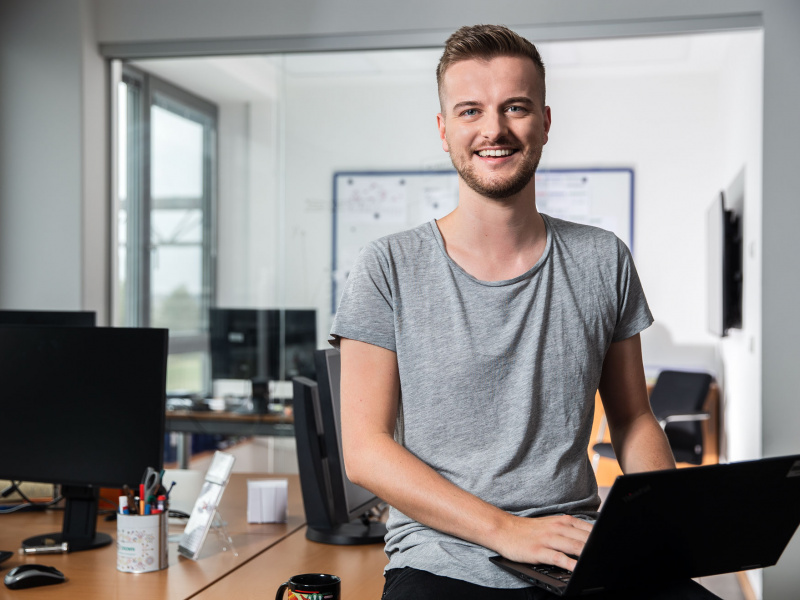 Junger Mann mit Laptop sitzt auf Tisch im Büro